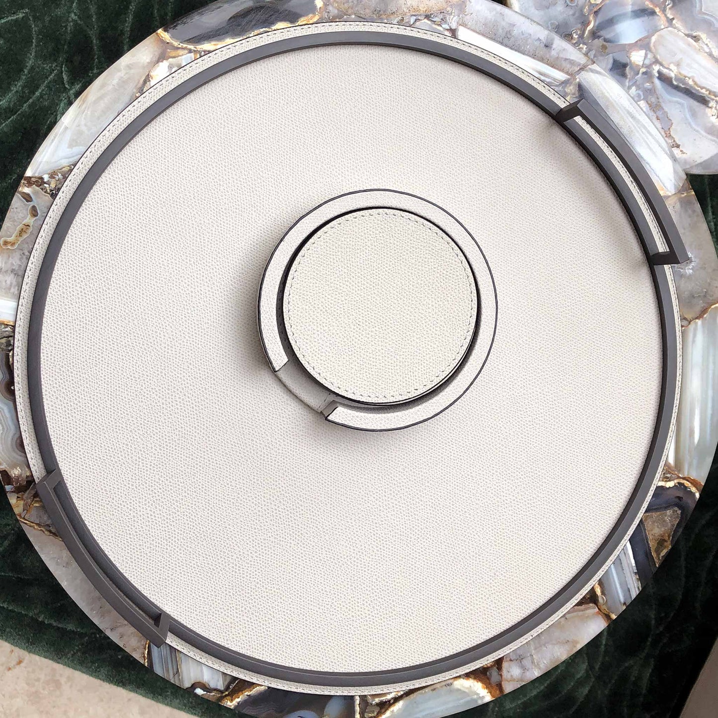 Lifestyle image of light grey luxury Italian leather coasters in holder and matching tray with bronze handles on a luxury marble accent table with silk green rug.