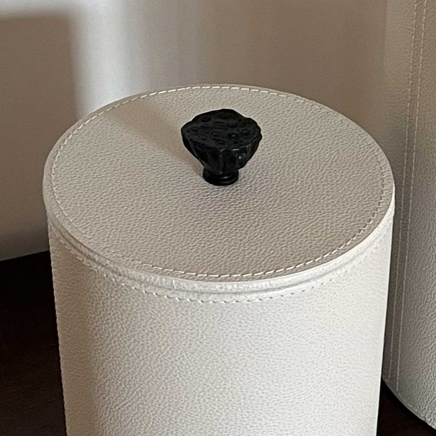 Close up lifestyle image of light cream leather cylinder box with cast brass handle