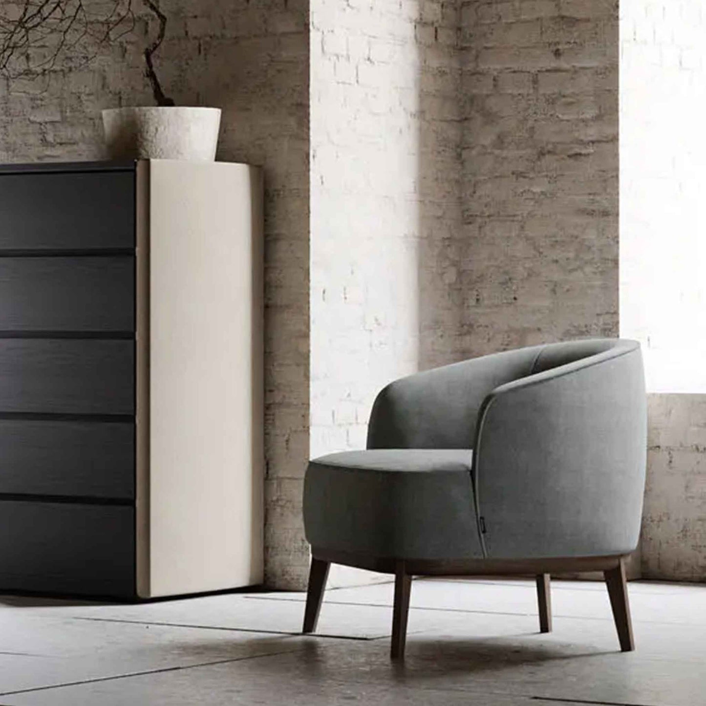 Lifestyle image of modern and minimal tub style armchair in grey velvet upholstery. Shown in minimal apartment with white brick walls.