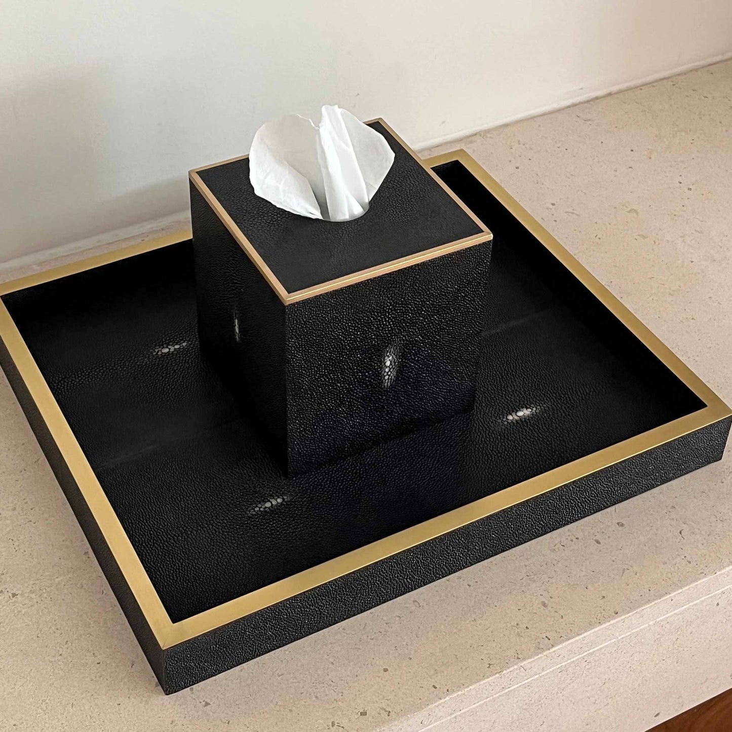 Lifestyle image of black luxury shagreen tissue box and tray with brass trim. Displayed on luxury stone mantel.
