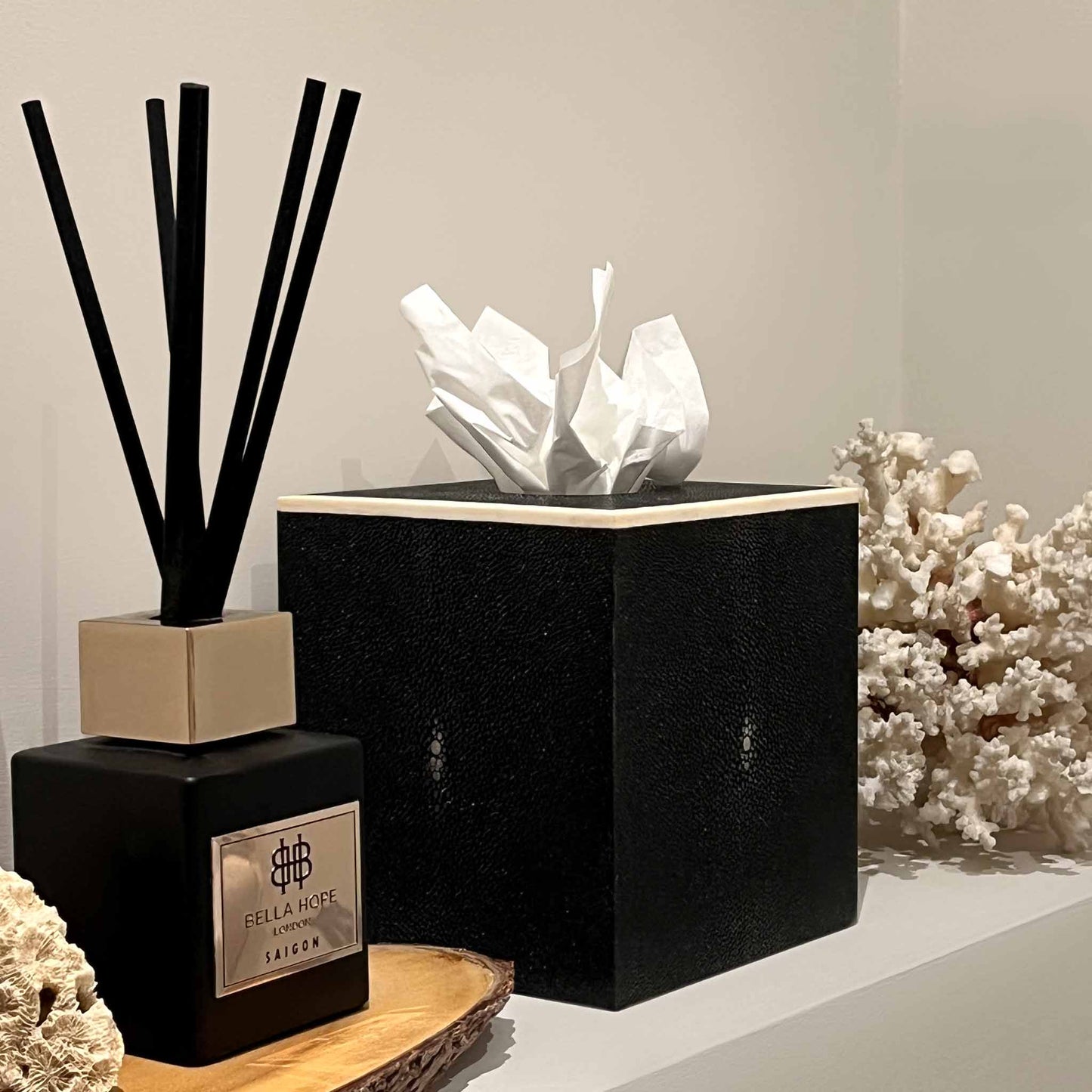 Lifestyle image of square black shagreen luxury tissue box with white bone trim. Displayed in a bathroom with a matching reed diffuser