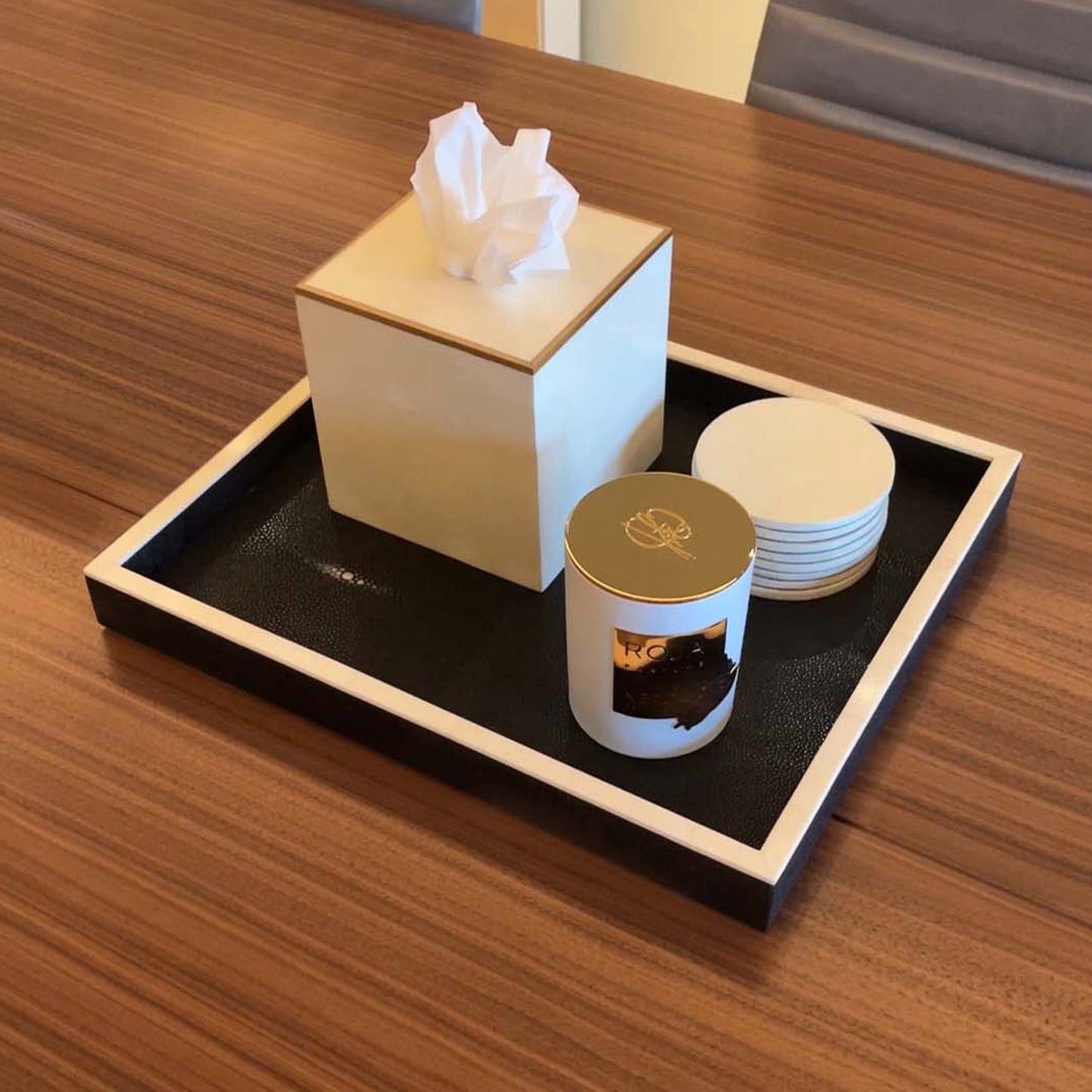 Lifestyle image of black shagreen rectangular tray with white bone trim displayed with matching parchment coasters and parchment square tissue box trimmed in brass. Displayed in a luxury office conference table with a candle