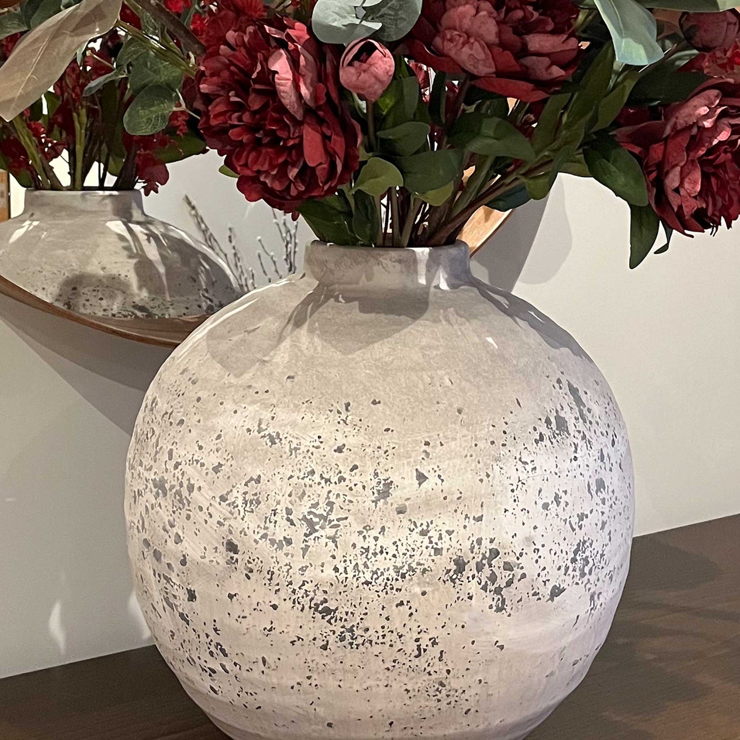 Lifestyle close up of large rustic and stone effect spherical ceramic vase with faux flowers.