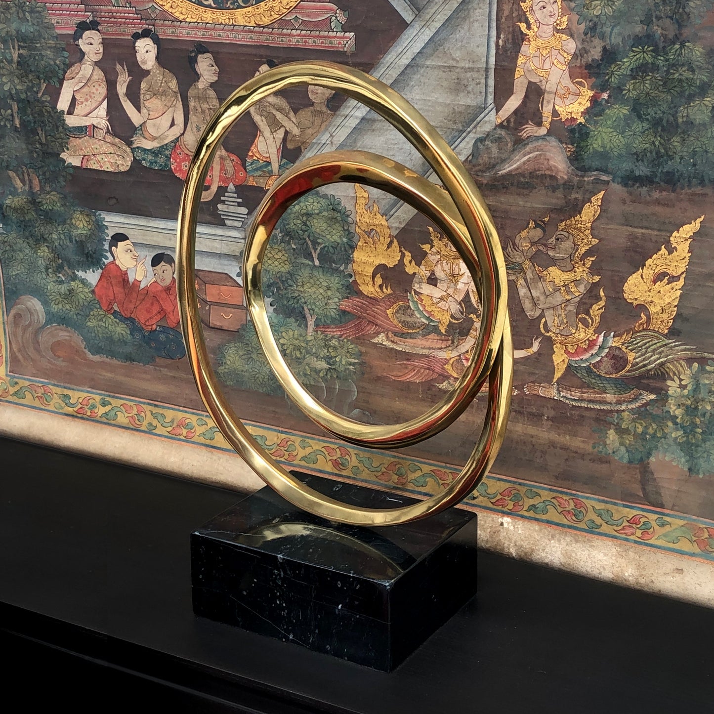 Lifestyle image of luxury round bronze decor Infinity Sculpture with marble block base, displayed against a Chinese tapestry