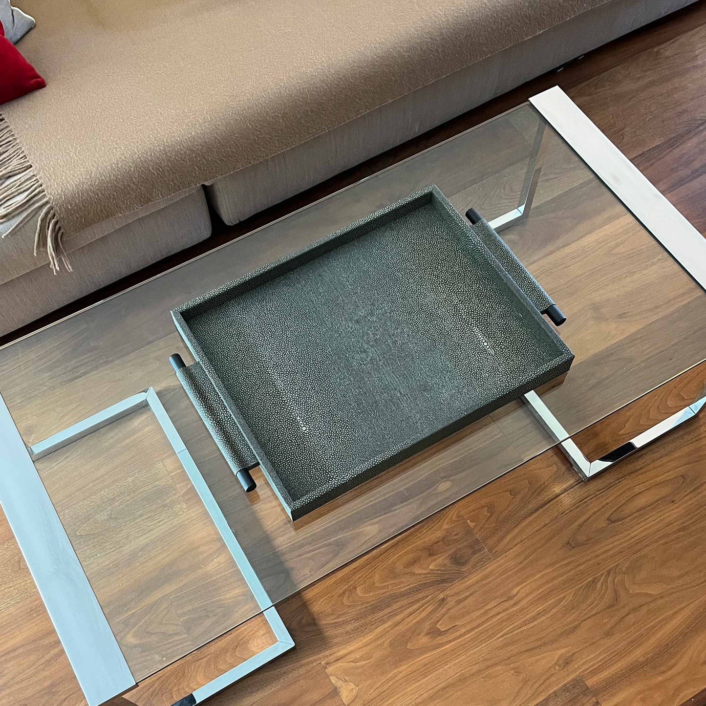 Lifestyle image of embossed grey shagreen textured leather, with wooden handles finished in carbon and leather wrapped. Shown on modern glass and chrome table with expensive wooden floor, next to sofa with cashmere throw and red cushion.