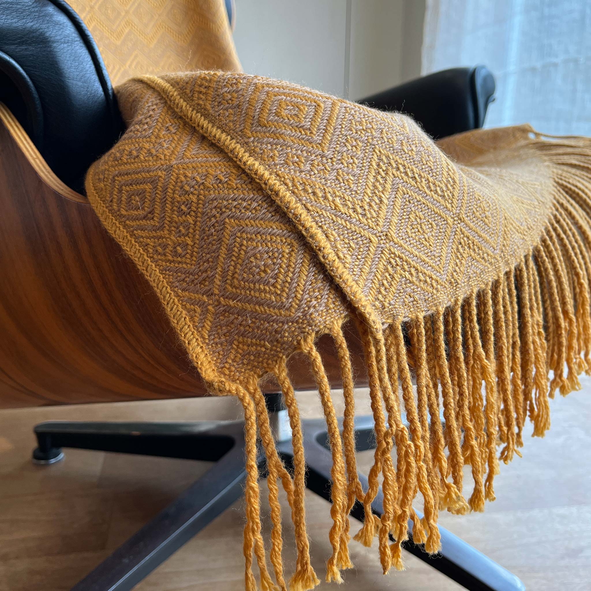 alpaca throw and blanket on eames chair with beautiful golden yellow saffron and camel geometric woven pattern and twisted long fringe