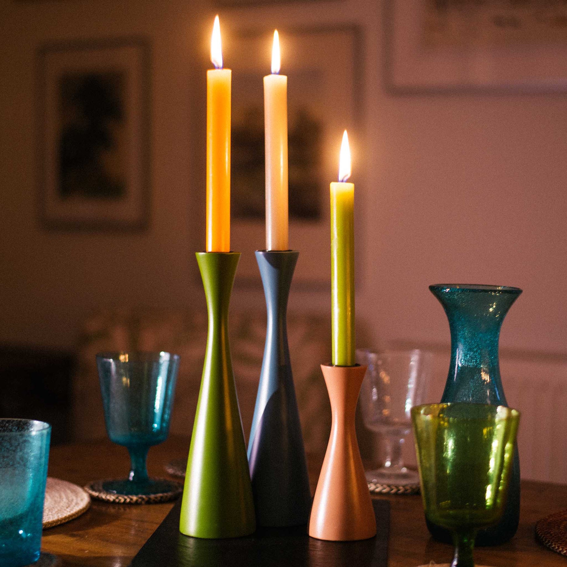 Lifestyle image of three minimal green, blue and rose pink candleholders. Displayed on a table setting with romantic candlelight.