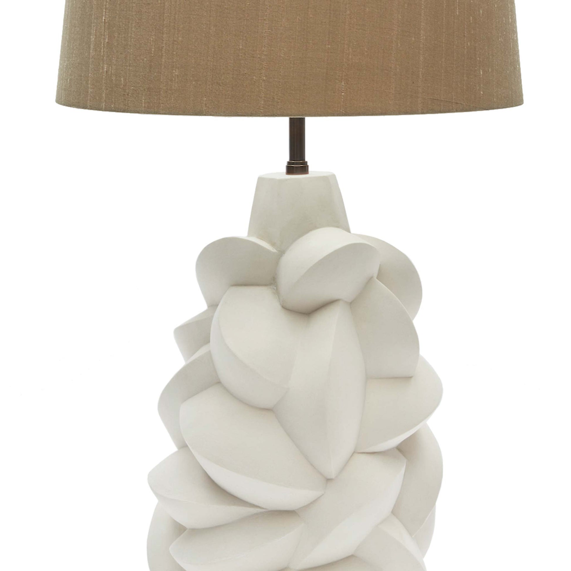 Close up art deco style table lamp with a jesmonite plaster body comprising of fragments and facets, resembling cubist sculptures. It is shown with a beige tapered linen lampshade