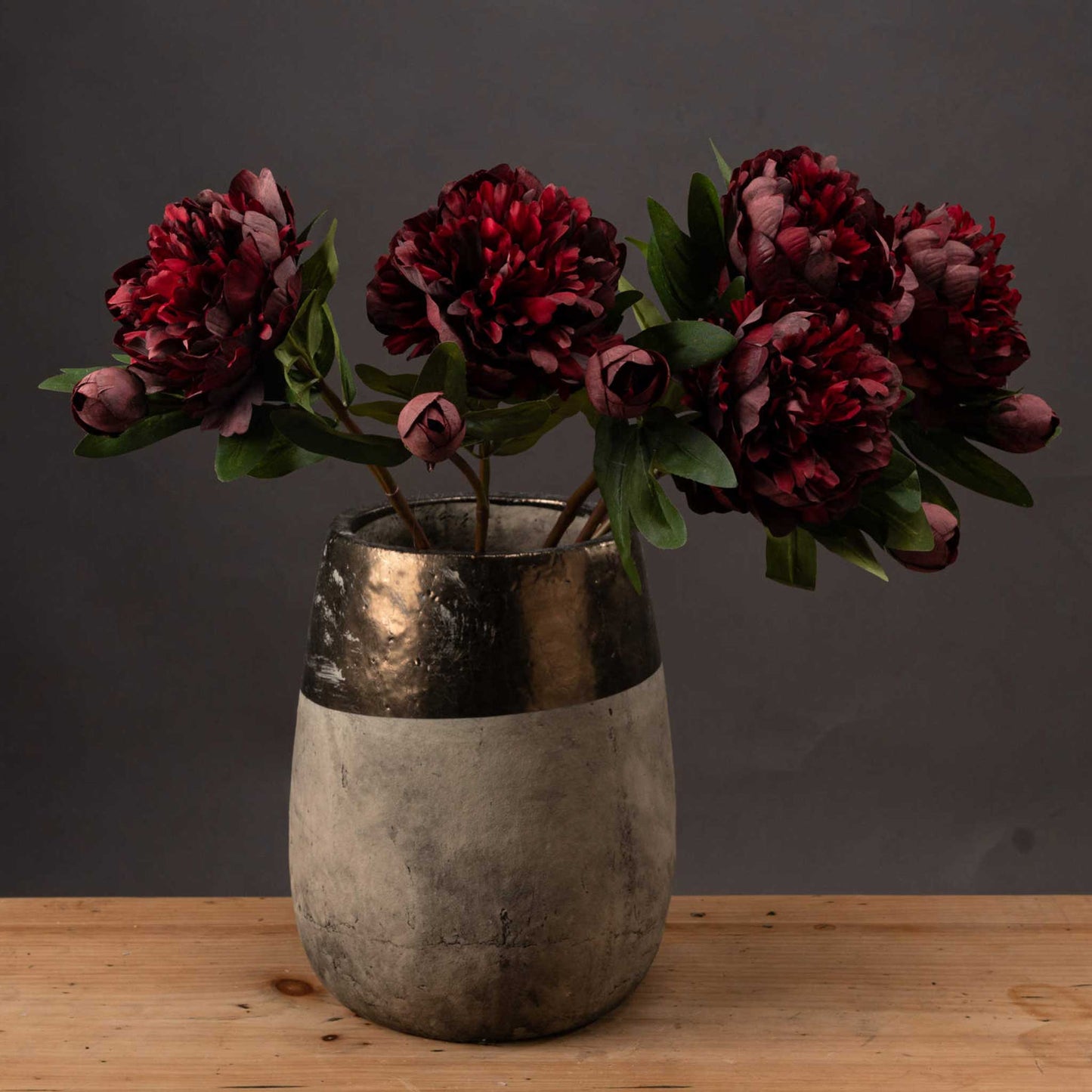 Lifestyle image of stone effect vase with gold rim and bunch of dark, rich red faux peonies