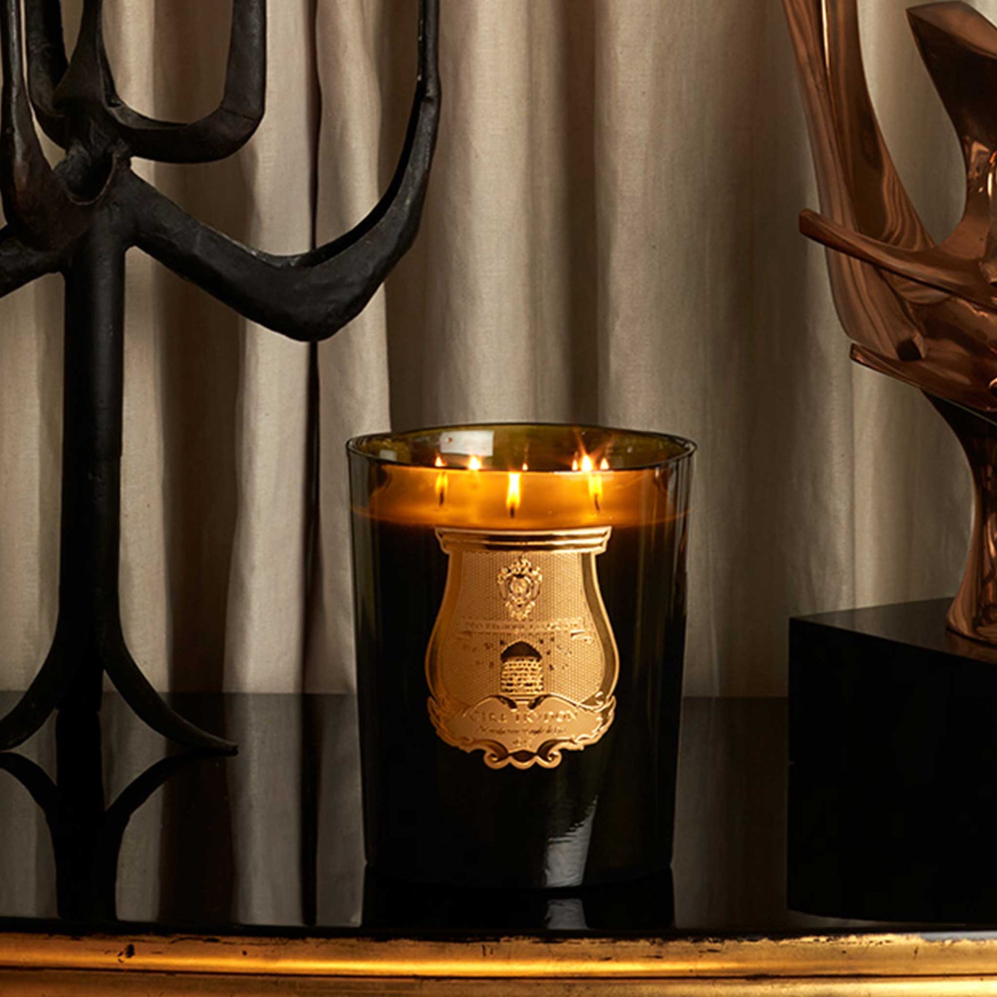 lifestyle image of a lit green jar cire trudon candle on a table