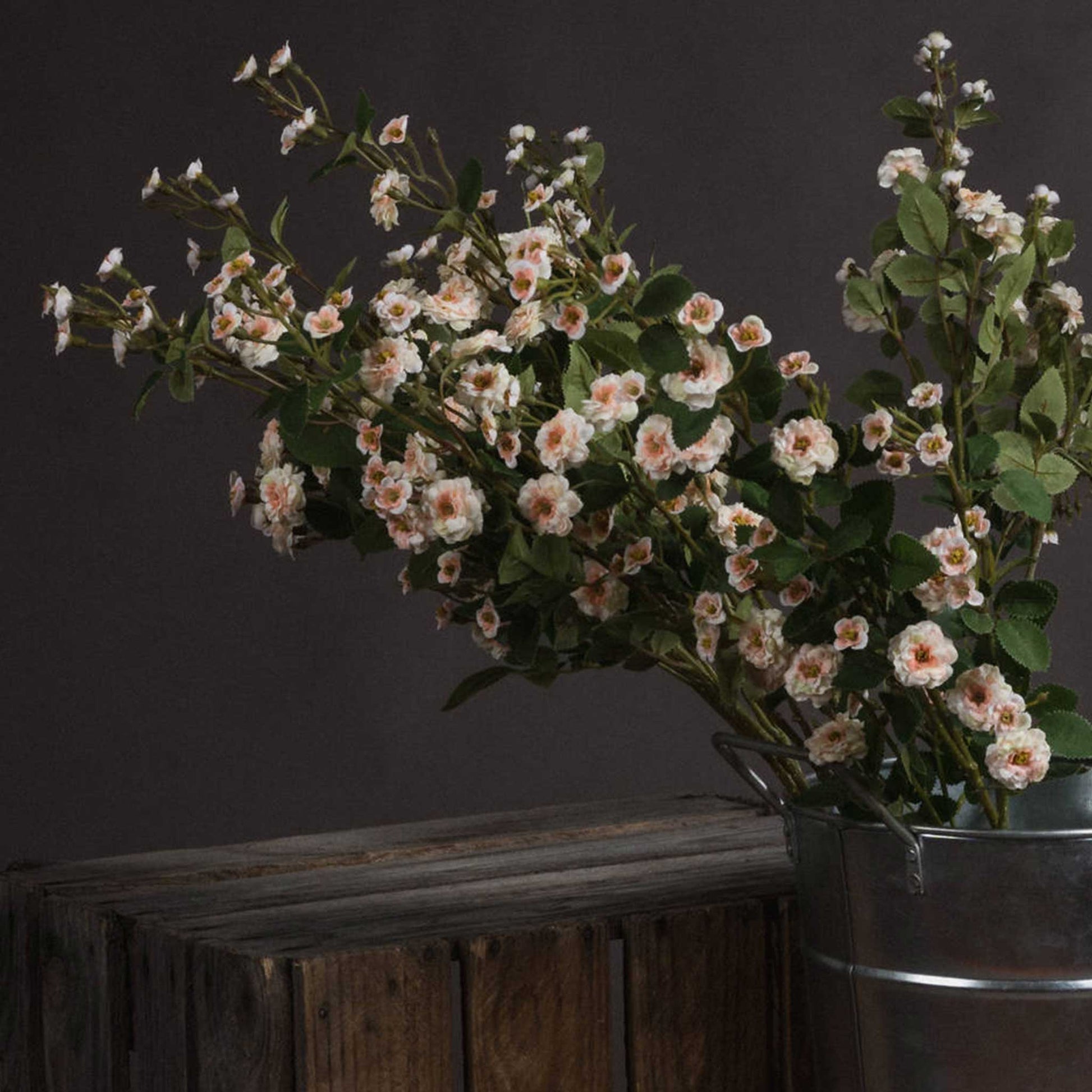 Lifestyle image of a bunch of miniature faux cream wild meadow roses. Displayed in a metal bucket and rustic setting.  