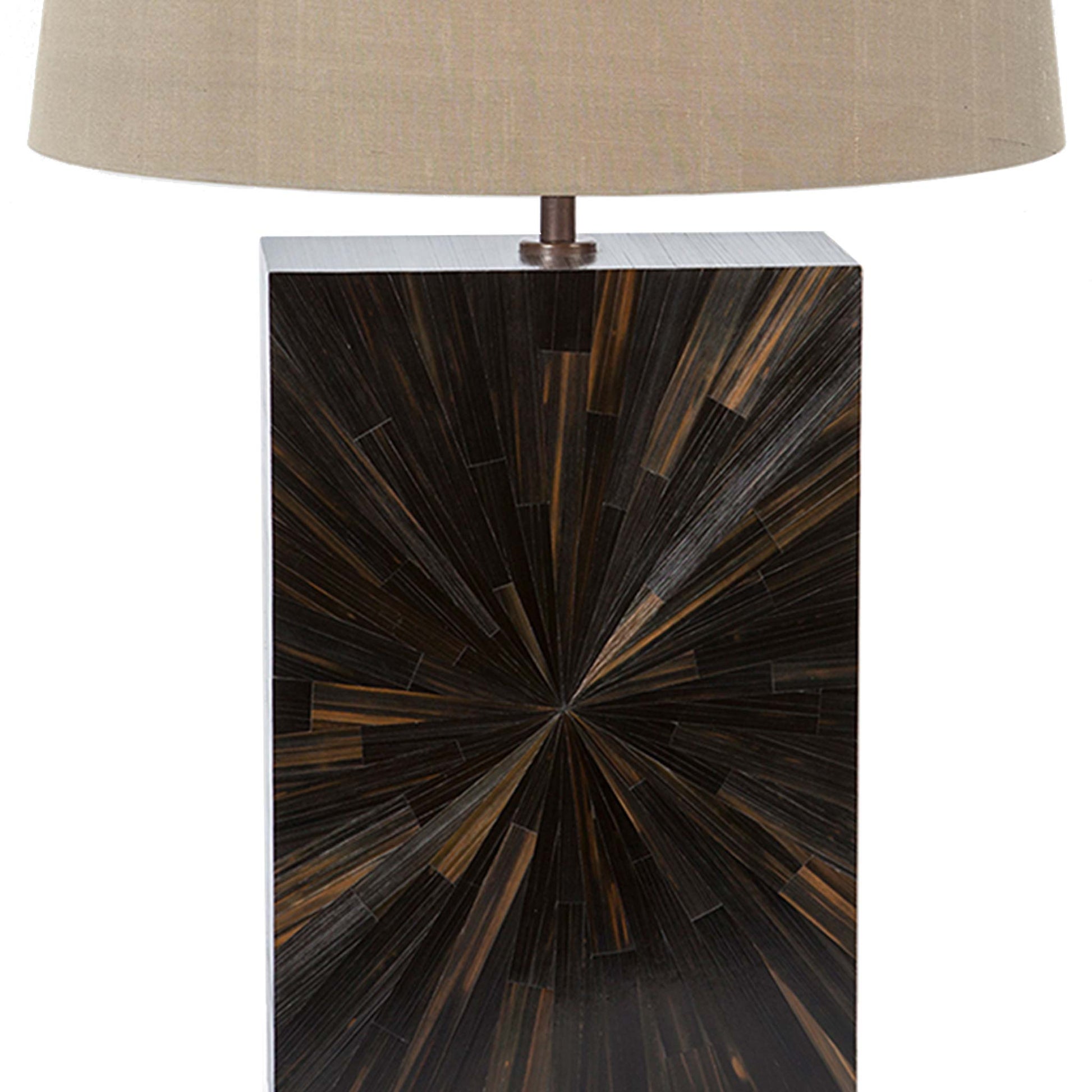 Close up of straw marquetry lamp with a starburst pattern in a minimal rectangular block design in dark brown and black tones the lamp is shown with a  beige tapered linen lampshade