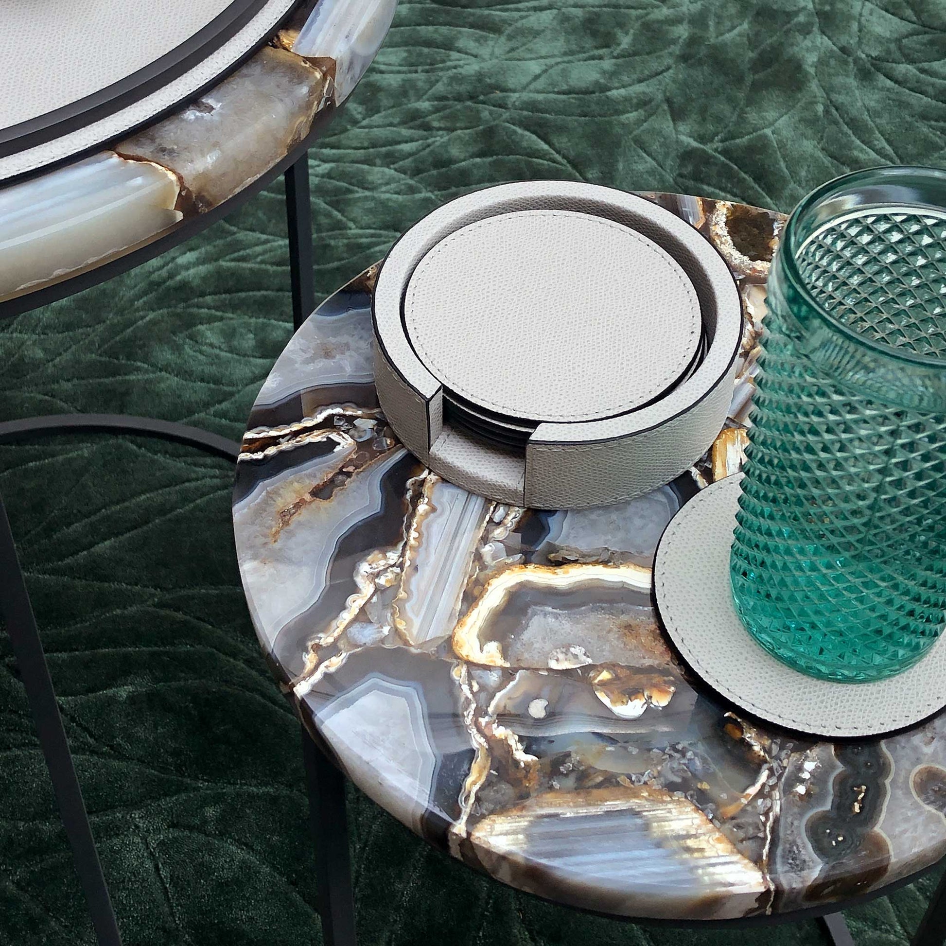 Lifestyle image of light grey luxury Italian leather coasters in holder on a luxury marble accent table with silk green rug.