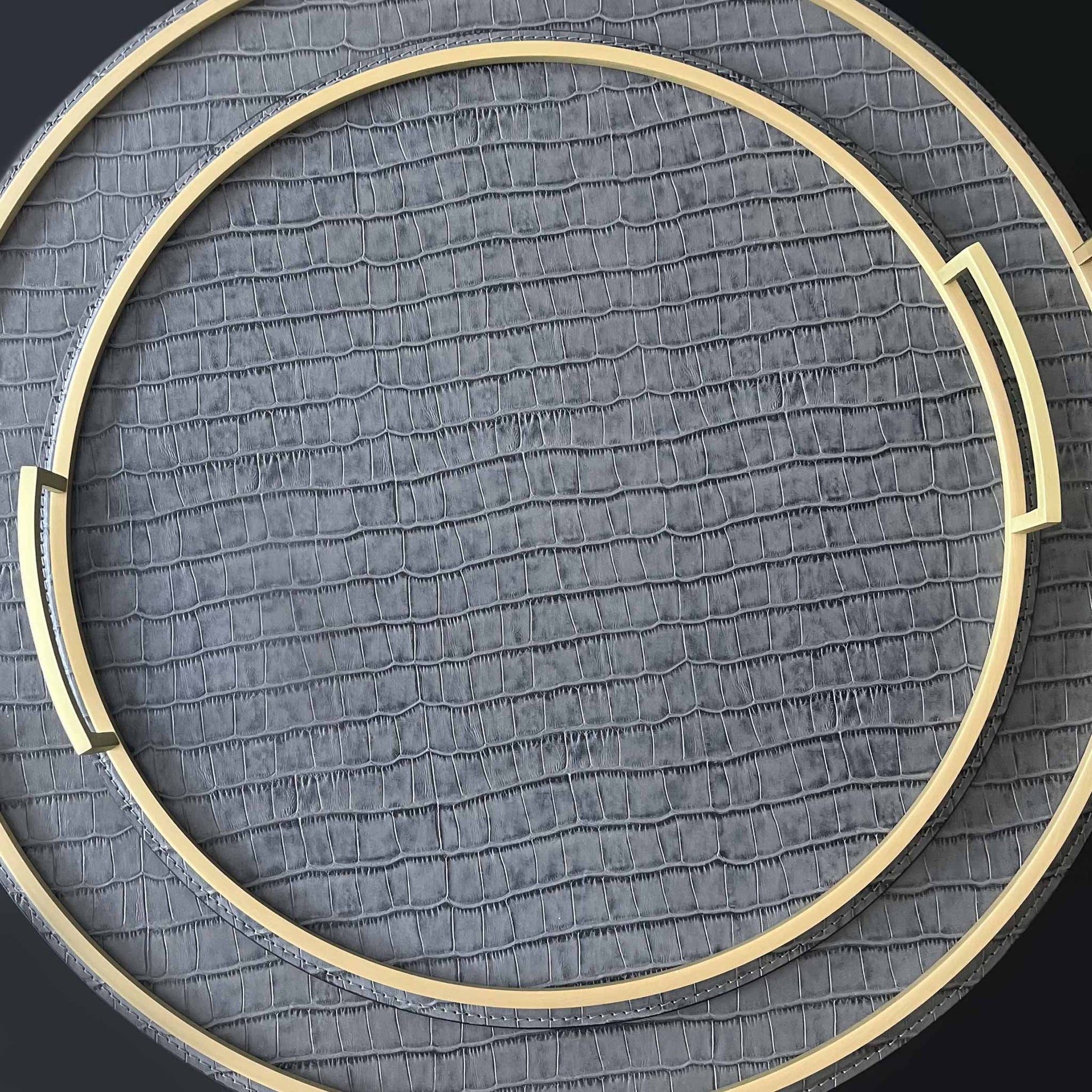 Close up of round grey crocodile textured Italian leather tray with brass handles. Displayed with two sizes stacked together. Seen from above