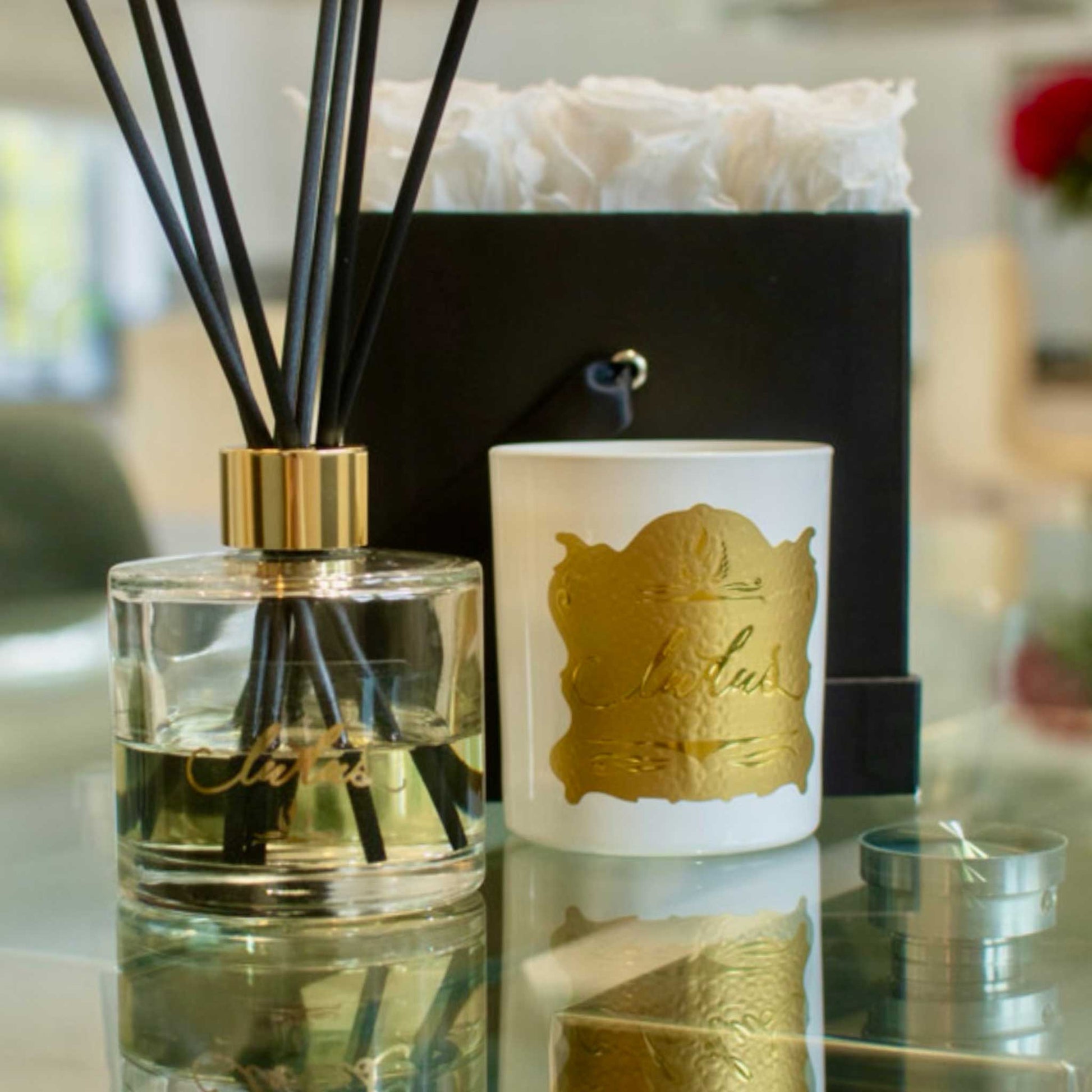 Lifestyle image of Oud Ludus candles displayed a luxury reed diffuser and white roses