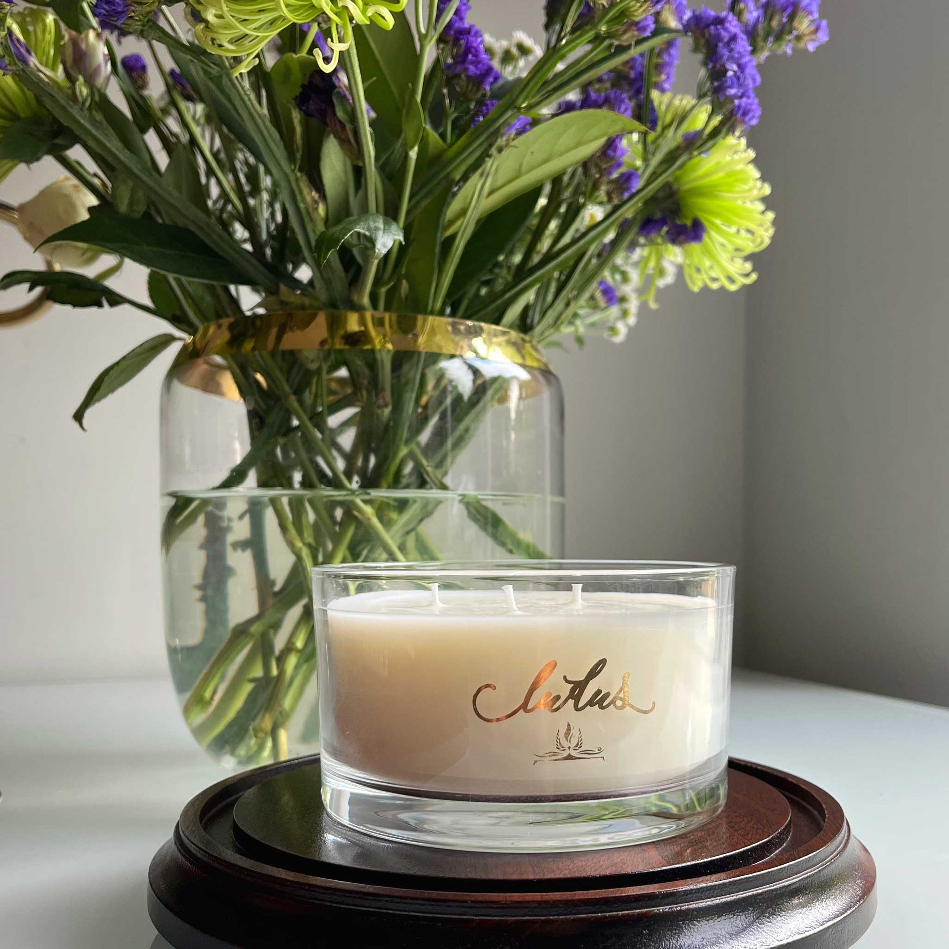 Lifestyle image of three wick luxury Ludus candle in stylish office. Displayed with a vase of wild flowers