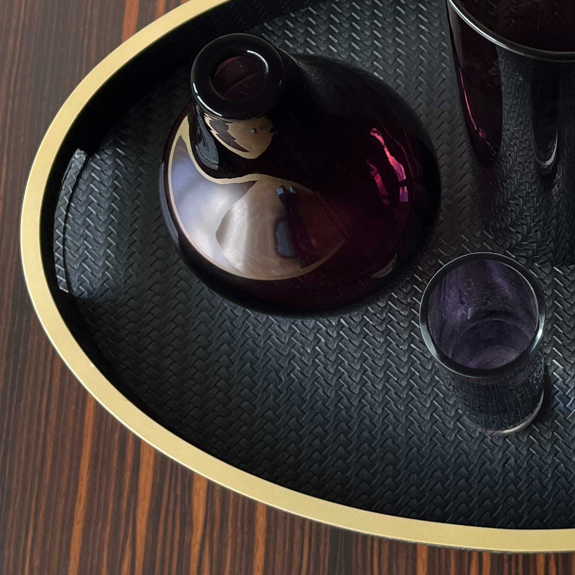 Lifestyle image of oval black textured leather with gilt trim and handles. Displayed with purple vases.