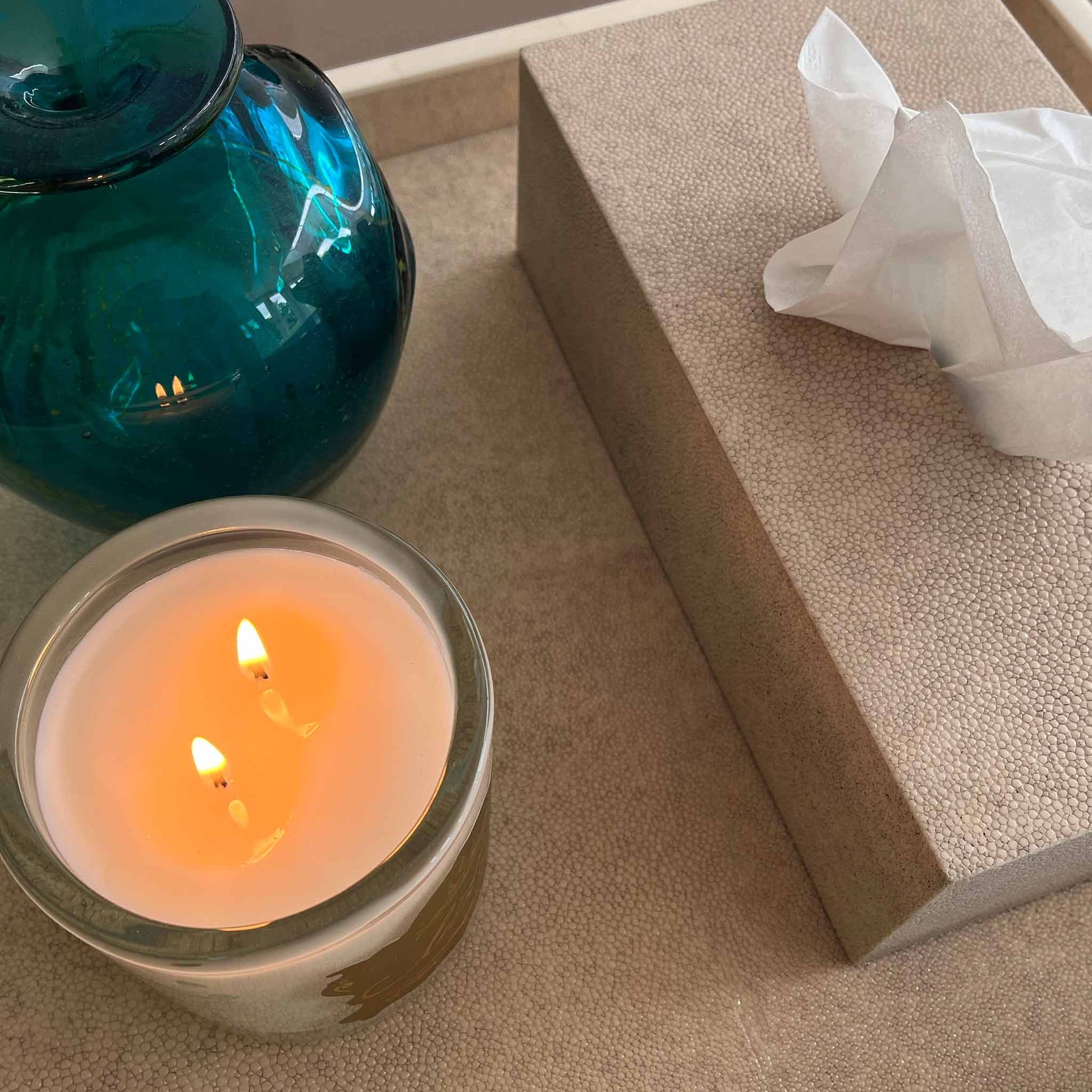 Close up of lifestyle image of rectangular natural shagreen luxury tissue box displayed on a matching shagreen tray with a lit candle