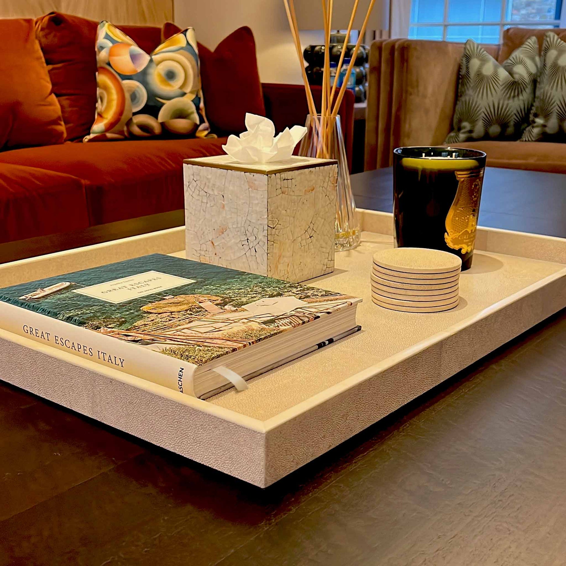 Lifestyle image of natural shagreen rectangular tray with white bone trim displayed with matching coasters, luxury candle and a shell and brass square tissue box. Set in a luxury living room.