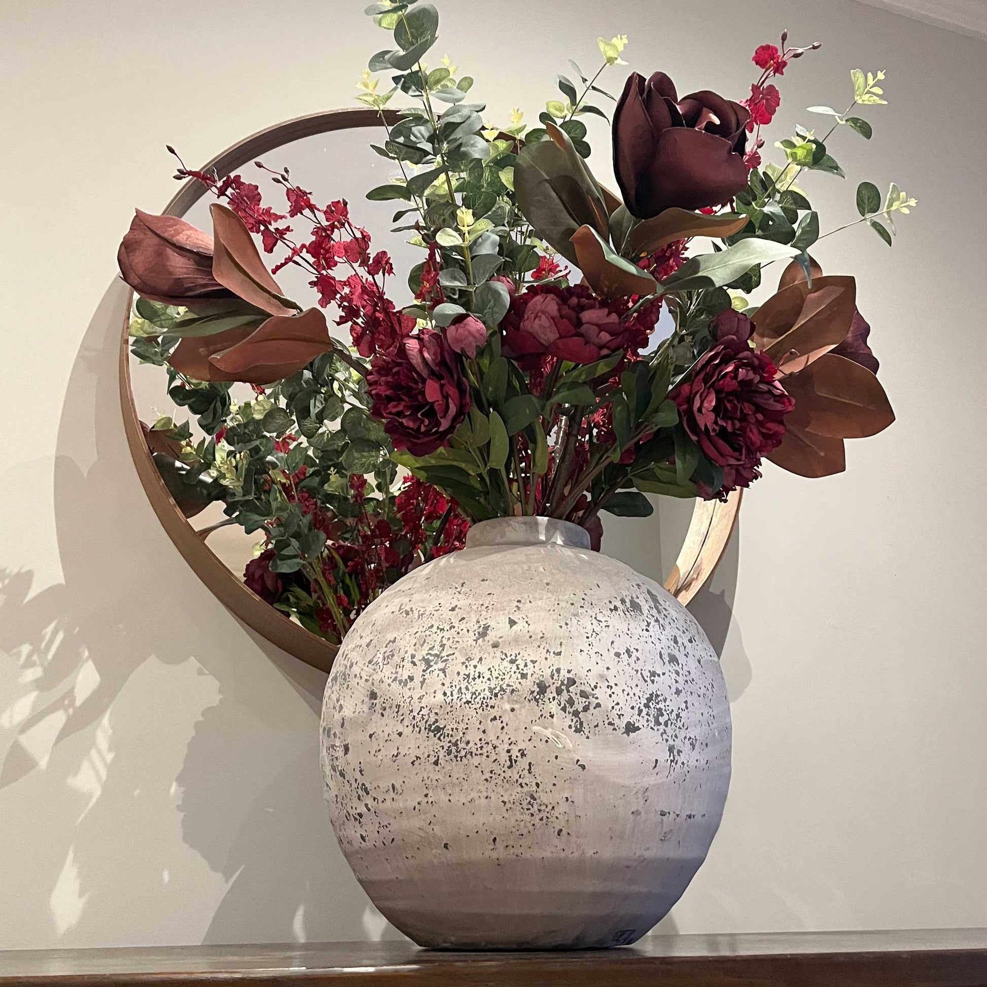 Lifestyle image of stone effect large spherical vase and mixed bunch of faux flowers.